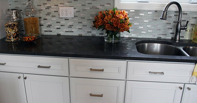 black counter top sitting on white cabinets with rectangular handles and subway pattern backsplash